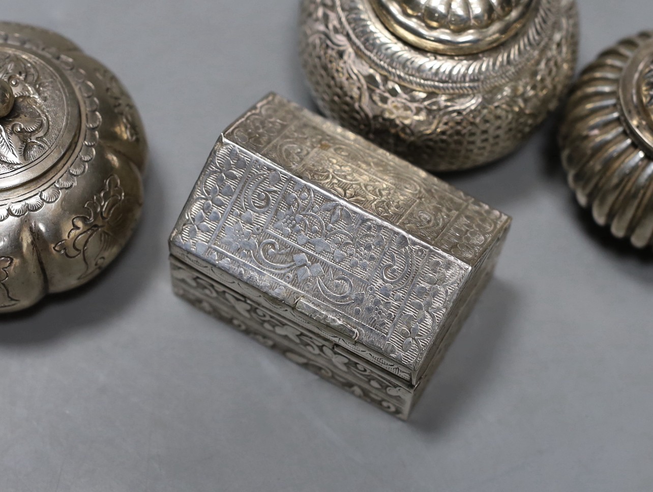 Five assorted 20th century Indian white metal circular boxes and covers including betel nut boxes and one other house shaped box and cover, largest diameter approx. 71mm.